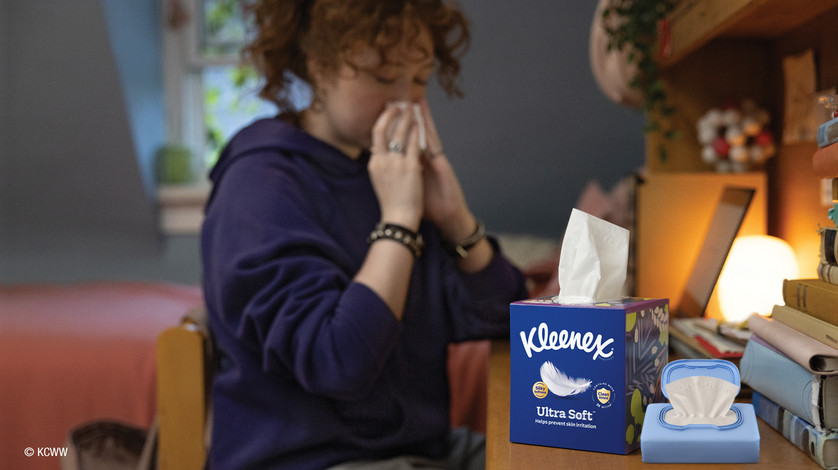 A woman blowing her nose into a Kleenex Ultra Soft tissue